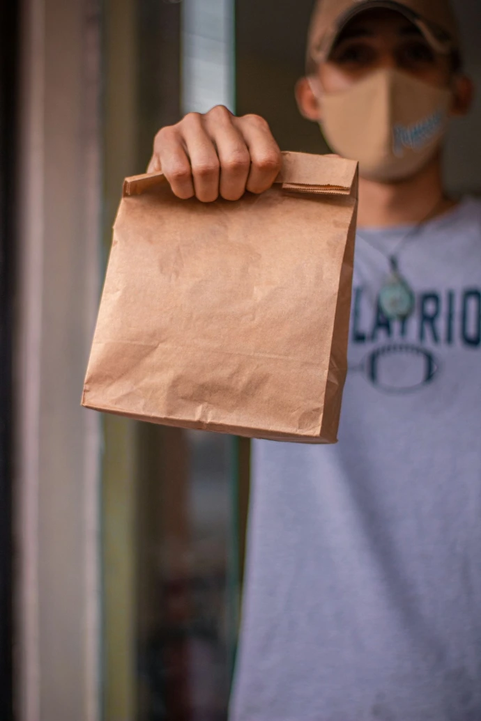 A man wearing a face mask holding a brown bag